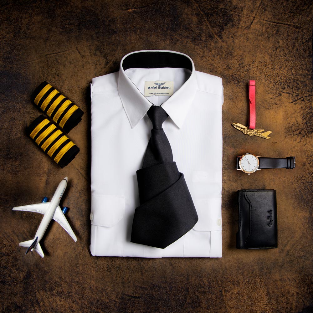 Image showcasing accessories of pilot. It consist of folded white  Standard Women's Pilot shirt., with a black half folded black tie, a watch, A Black wallet, Hand band, Yellow shoulder strip and a plane modal