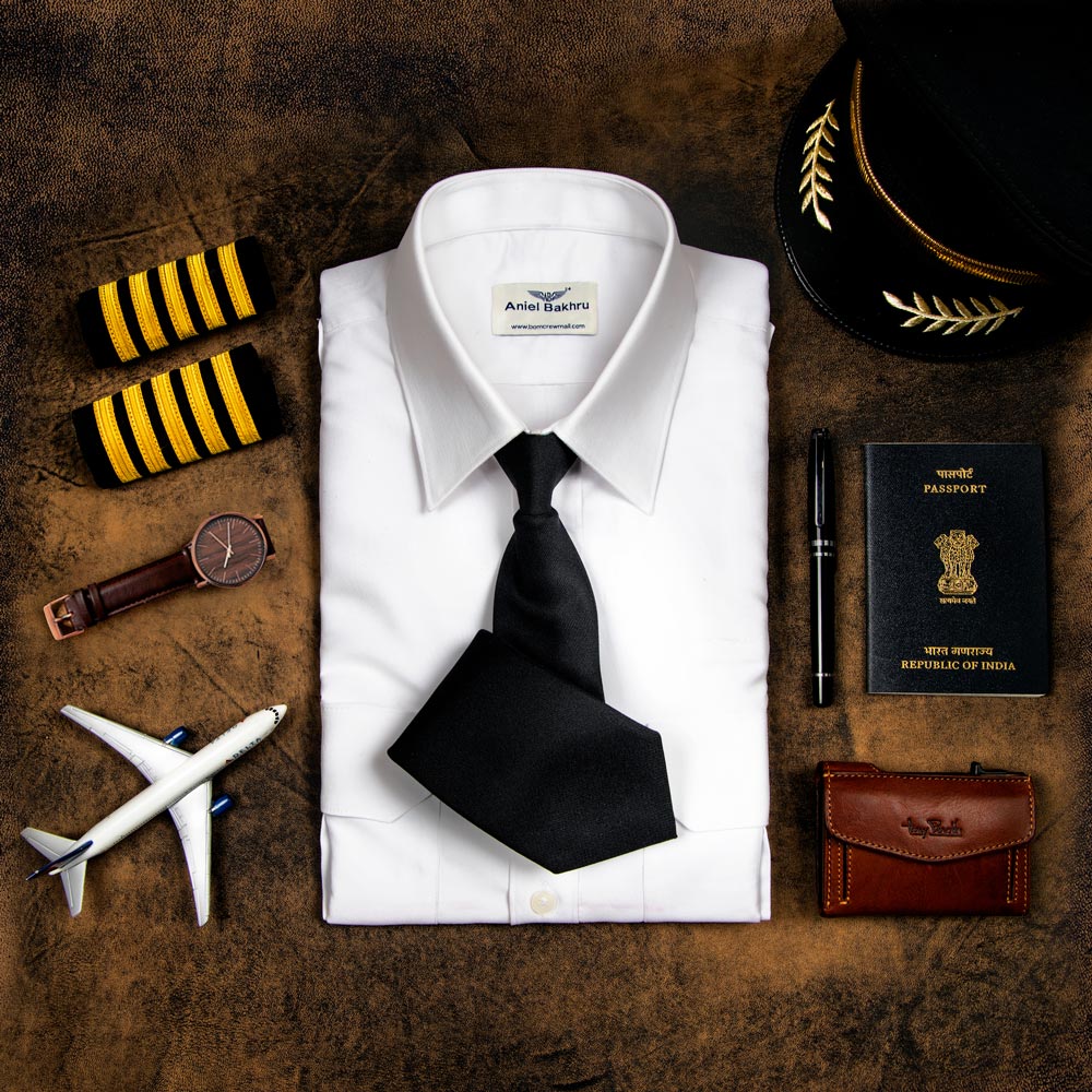 image showcasing accessories of pilot. It includes folded white Standard Pilot Shirt with black  half folded neck tie, a watch, brown wallet, pen, pilot yellow shoulder strip, passport , pilot cap and a plane modal