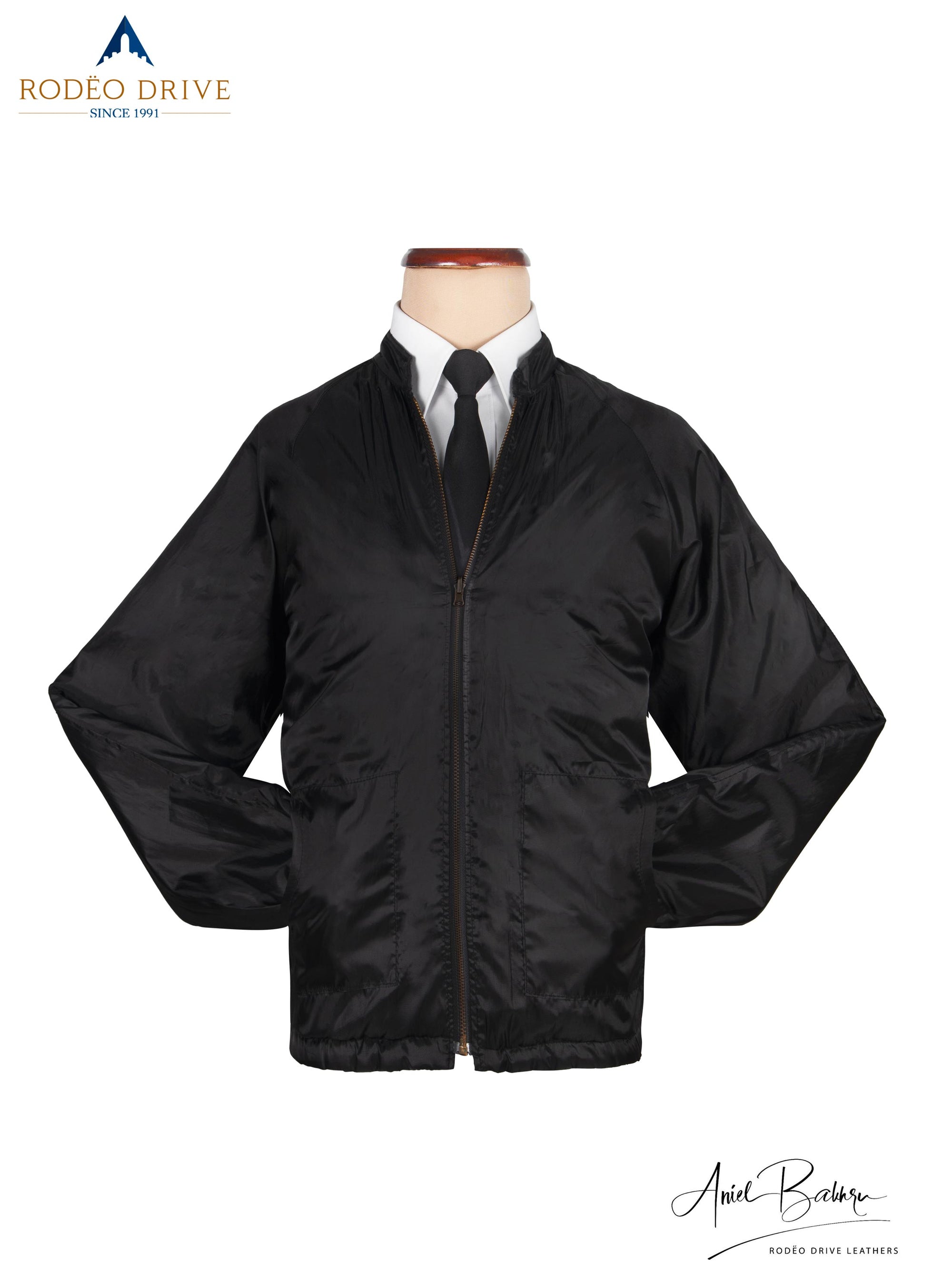 Image of plane black leather Jacket displayed on mannequin. A white shirt and neck tie is tucked in. Both the hands are tucked inside slit pockets. Classic way to wear the jacket
